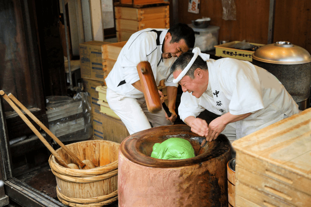 Two men making what is mochi (yomogi.mugwort) flavor in a traditional pestle.