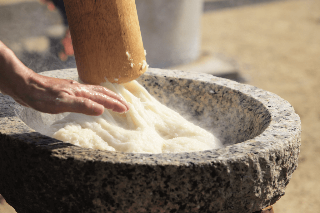 Someone making what is mochi in a large pestler.
