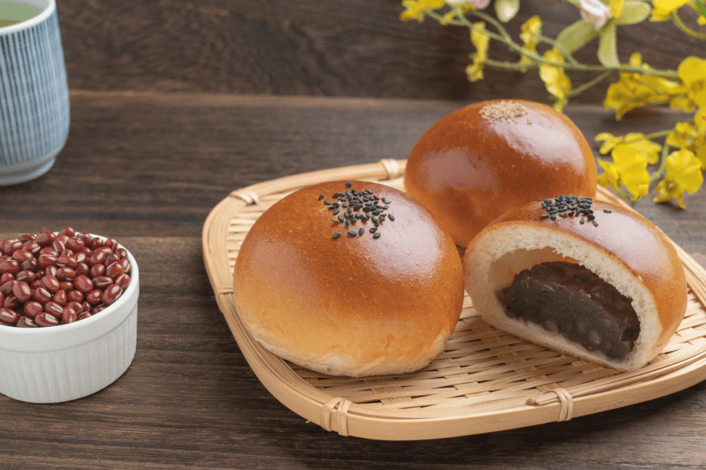 Red bean paste buns next to a bowl of azuki red beans.