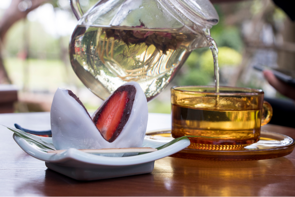 A strawberry daifuku infront of a tea pot.