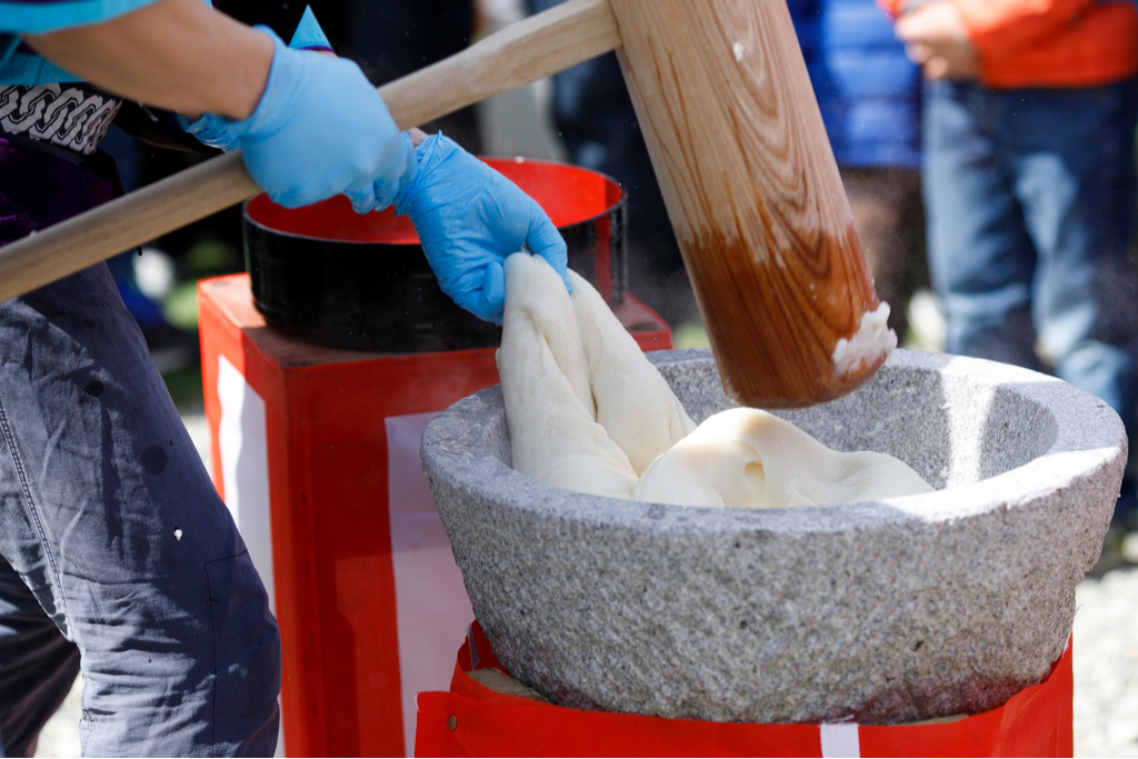 An artisan pounding mochi with mallets. This tradition is a part of mochi history. 