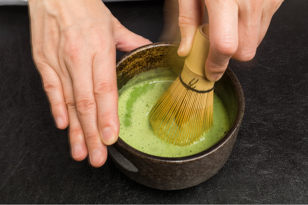 A pair of hands intensely stirring matcha tea for a Japanese tea ceremony.