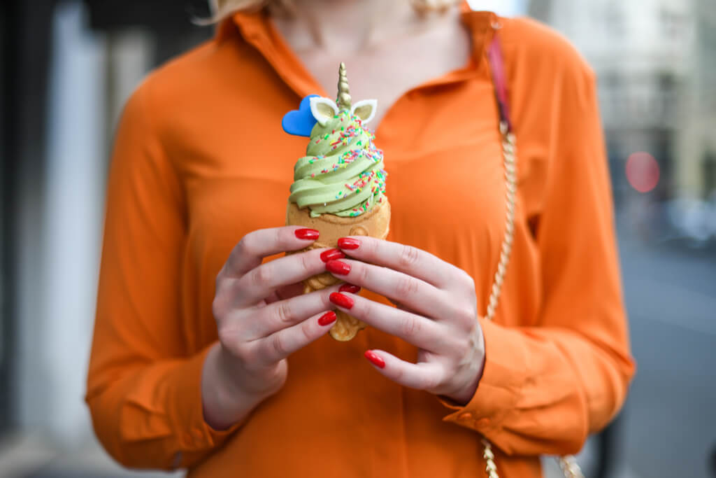A woman in an orange shirt holds taiyaki filled with ice cream topped with a unicorn horn and a blue heart