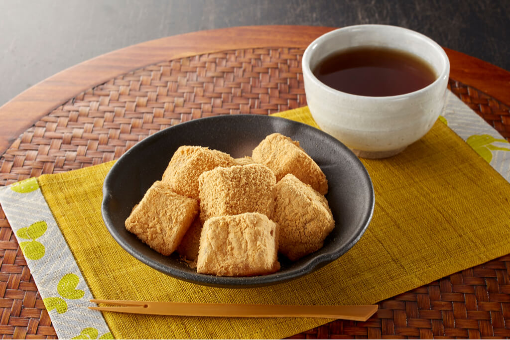 A small bowl of kinako-covered mochi next to a cup of tea.
