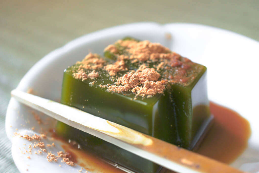 Green tea yokan topped with kinako on a plate with brown sugar sauce