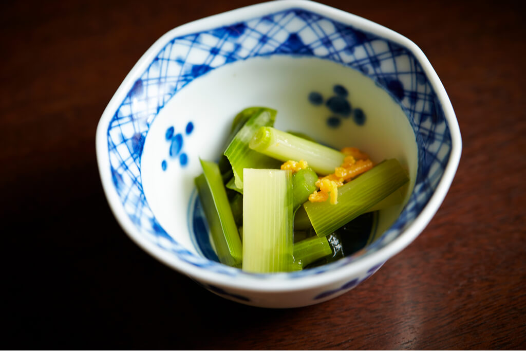 A blue bowl of celery and green onions with an orange vegetable on top and seaweed on bottom.