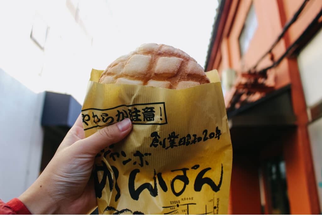 A hand holding up Japanese melon pan in the streets of Tokyo.