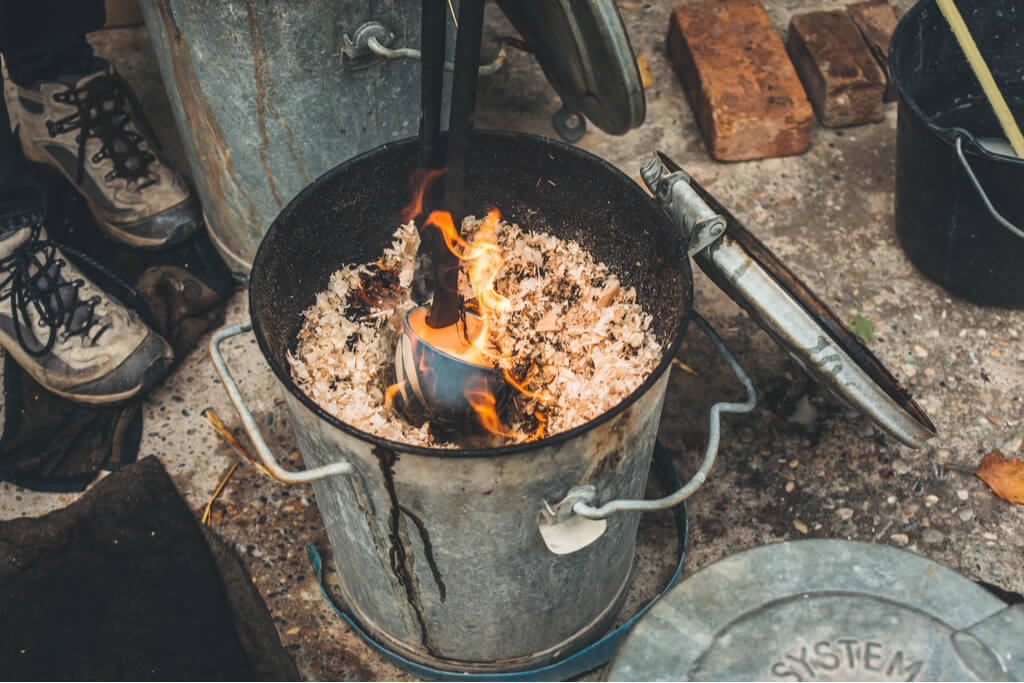 A raku ware bowl being fired inside of a bucket containing fire and wood shavings.