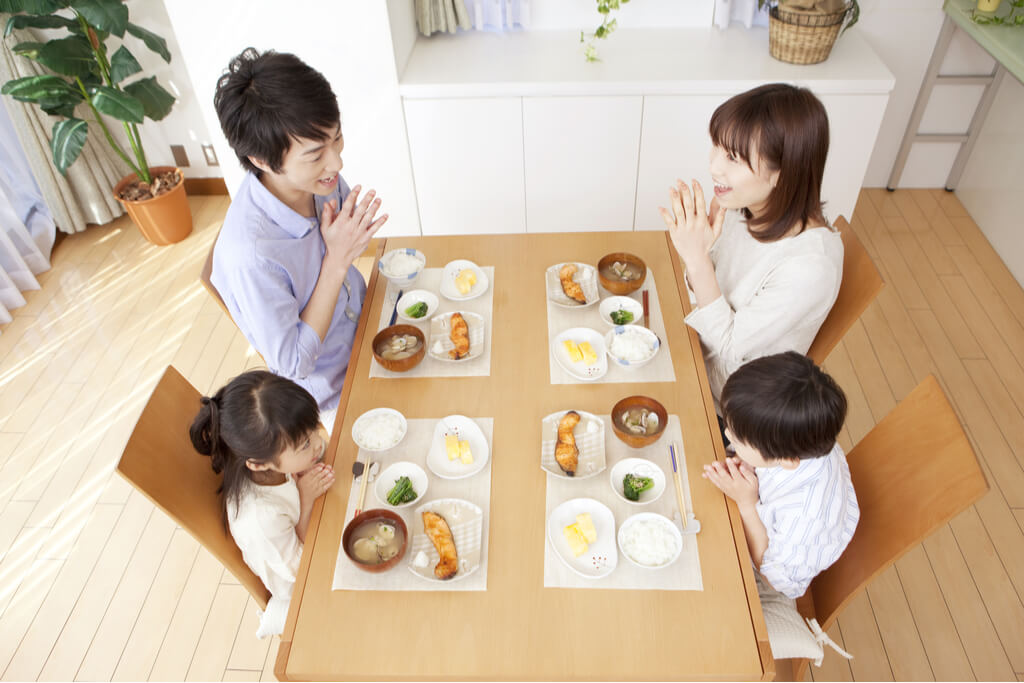 A family of four, (a father, mother, daughter and son) sit down to a traditional Japanese salmon meal.