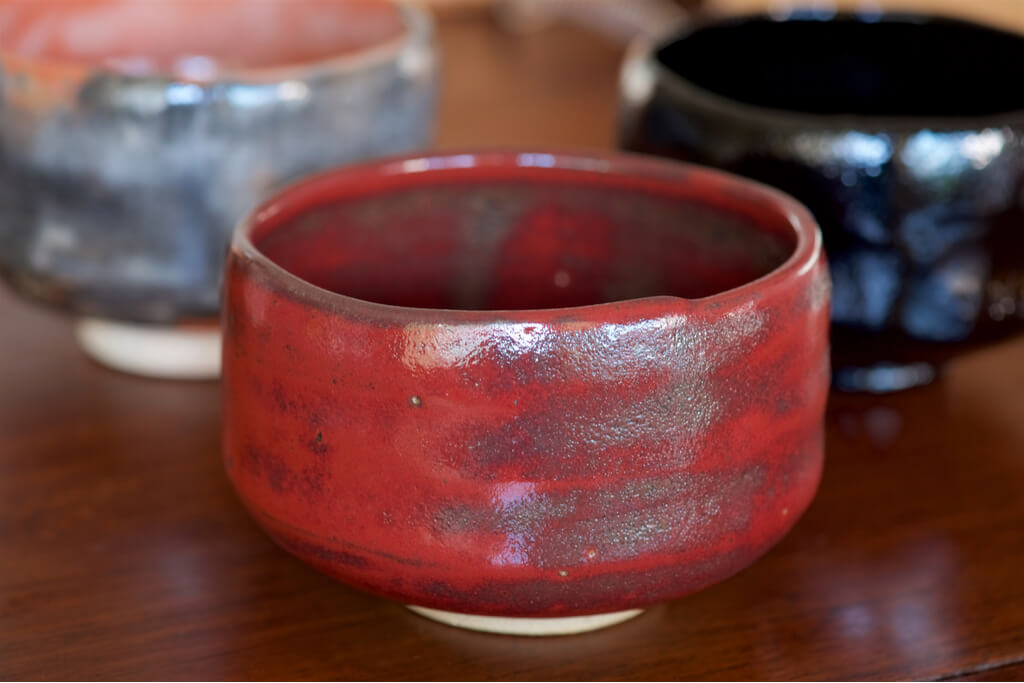 A red, grey and black chawan sit on a table.