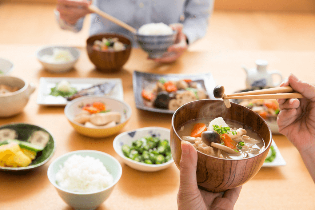 A person at the dinner table eating pork miso soup with chopsticks.