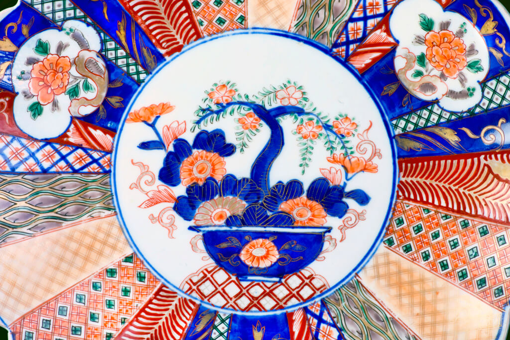 A close-up of an antique imari ware from Japan 1860 with an illustration of a tree among flowers in the middle of several patterns