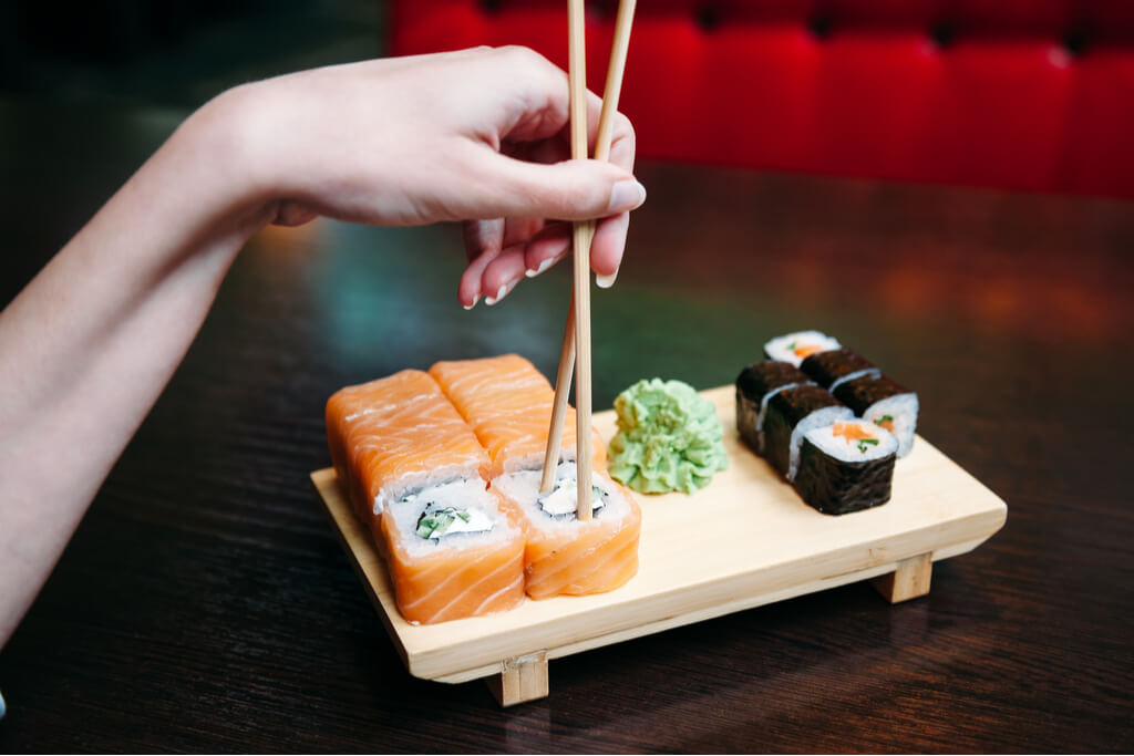 A woman's hand stabs a sushi roll with her chopsticks in a restaurant.