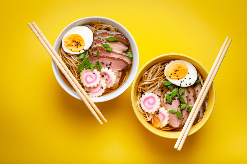 Two bowls of ramen with chopsticks laid across the bowls on yellow background
