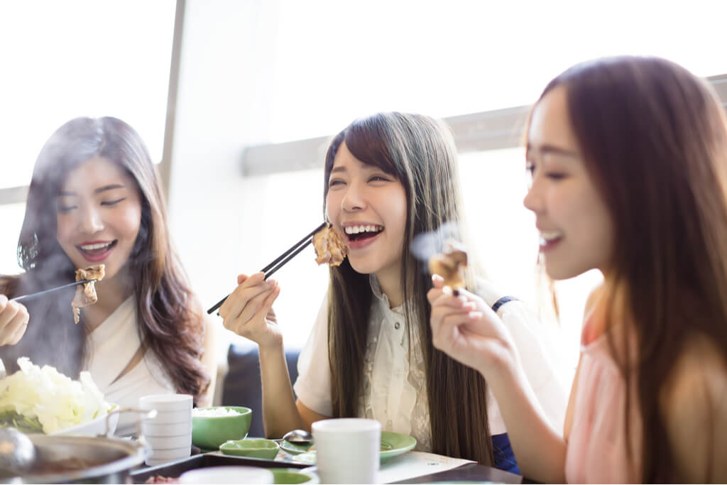 Three women enjoy eating yakiniku at a restaurant while smiling and laughing.