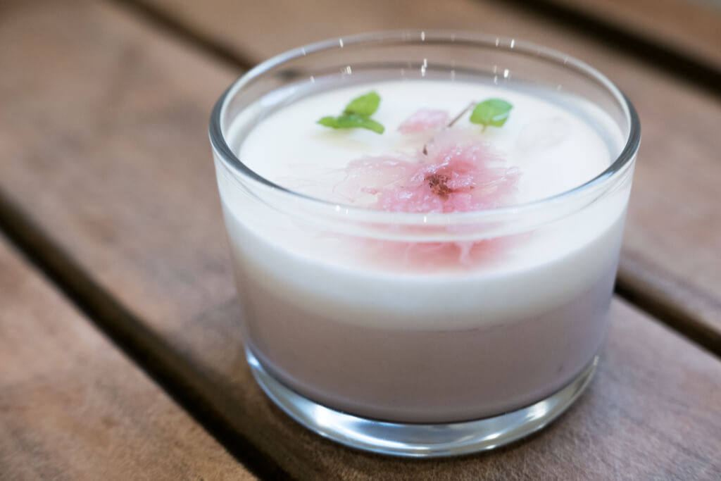 A cup of sakura-flavored milk pudding with plain milk pudding with sakura leaves on top on a wooden table