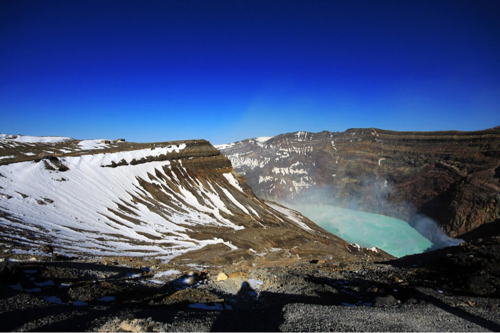 A picture of the top of the caldera of Mt. Aso with a pool of hot water steaming up and some snow around it