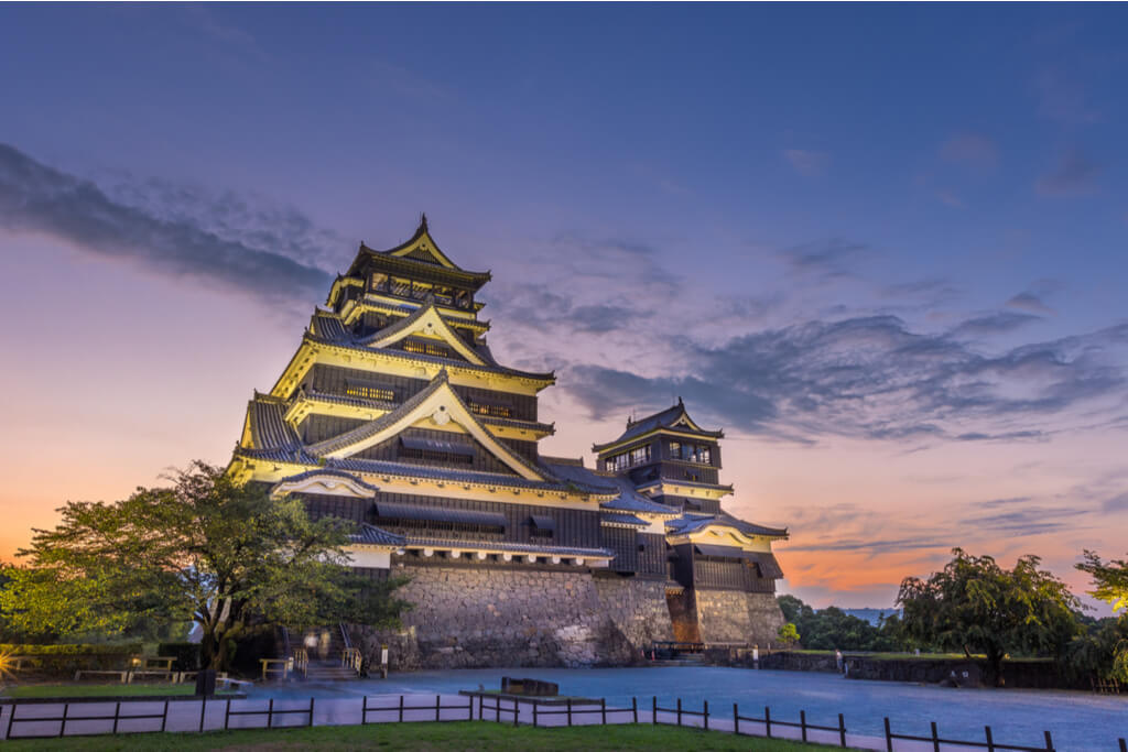 Kumamoto Castle sits with lights on it with a sunset in the background