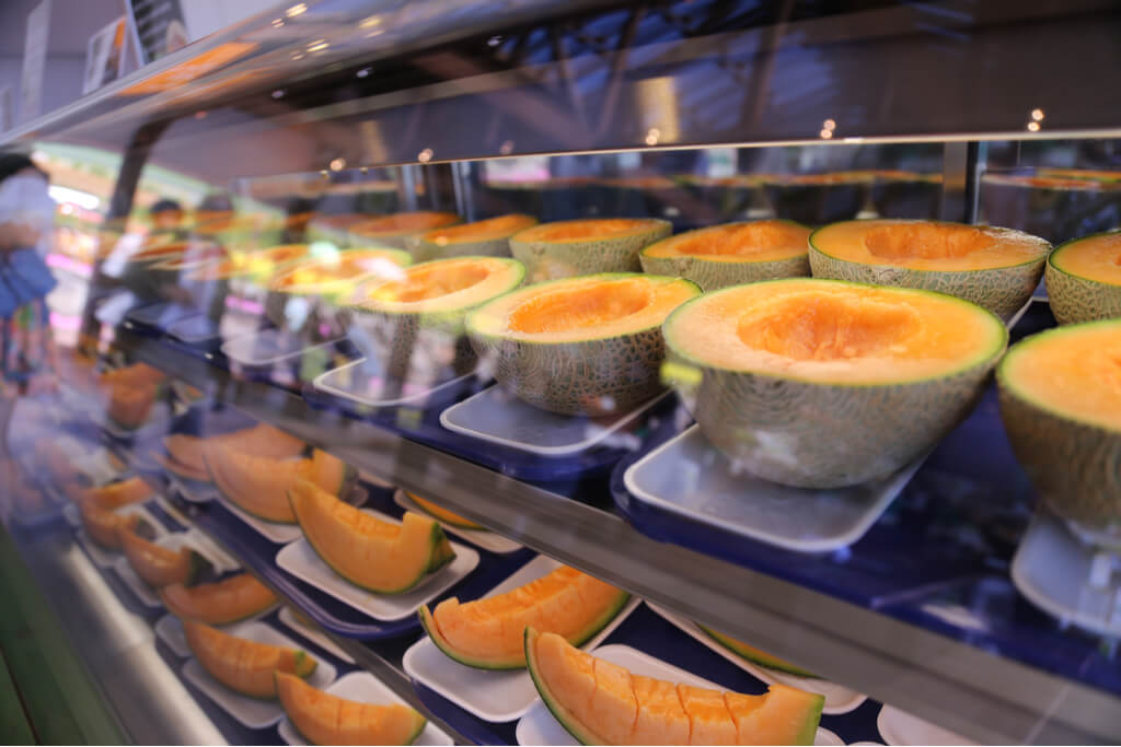 A case full of melon grown in Hokkaido at a farm with the reflection of people walking by