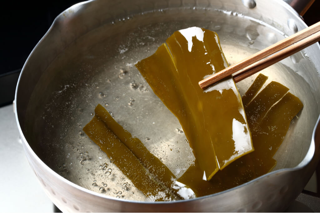 Pieces of kombu being picked out of a dashi made for ishikari nabe out of a steel pot by chopsticks.