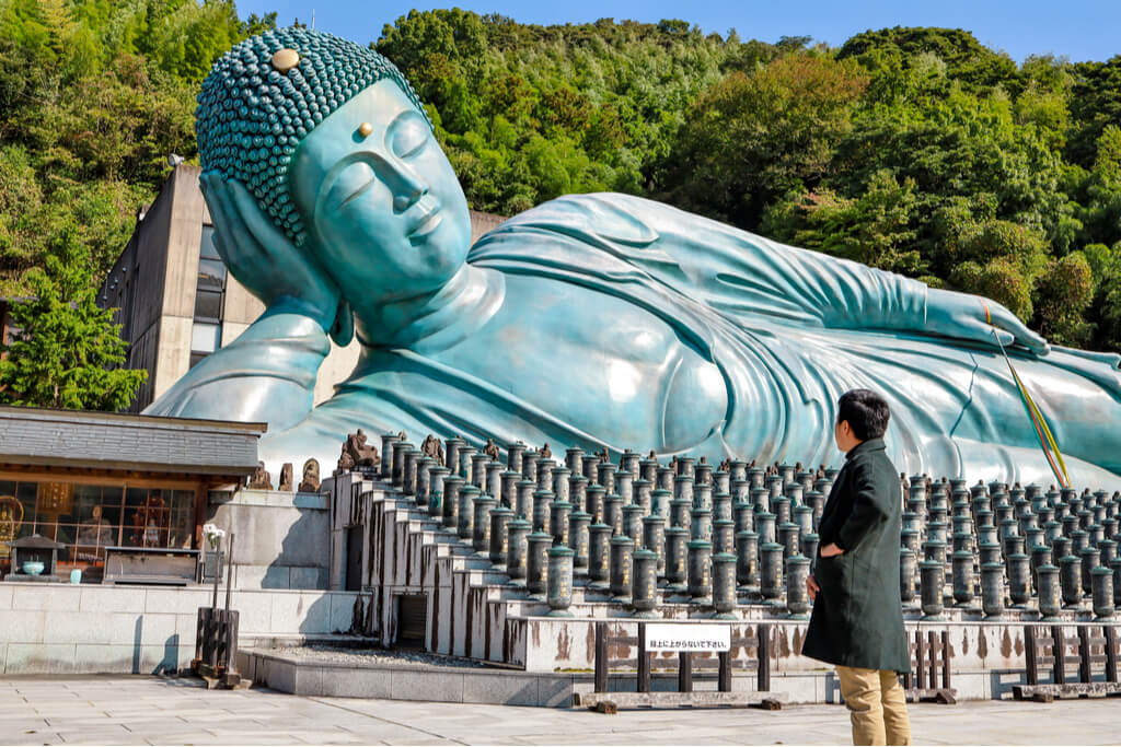 The Great Buddha of Nanzoin, Kyushu's most prominent Buddhist temple, sits behind other smaller statues as a man looks on