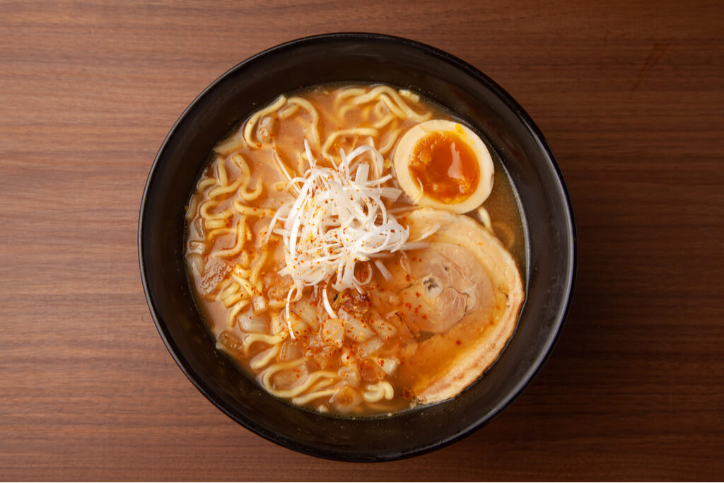 A bowl of Muroran curry ramen, a Hokkaido ramen type, with pork, red pepper, egg, and onion on top.