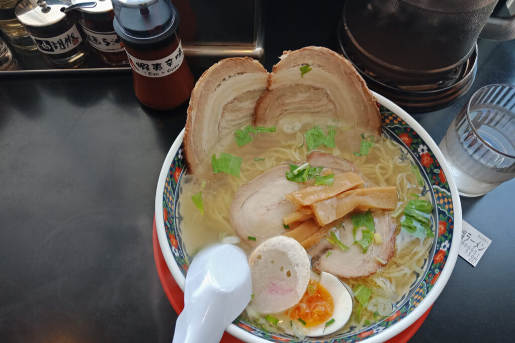 A bowl of Hakodate ramen, a Hokkaido ramen variant, with a clear broth with chashu, egg, and fish cake on top at a ramen restaurant