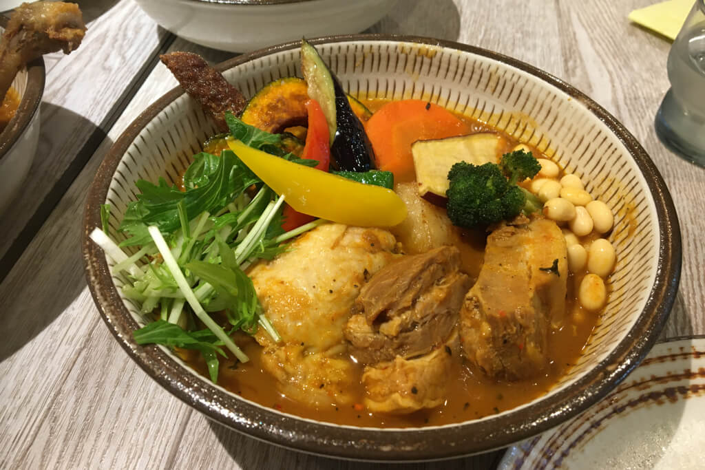 A bowl of soup curry, a Hokkaido food creation, with beans, meat, pumpkin, eggplant and other vegetables.