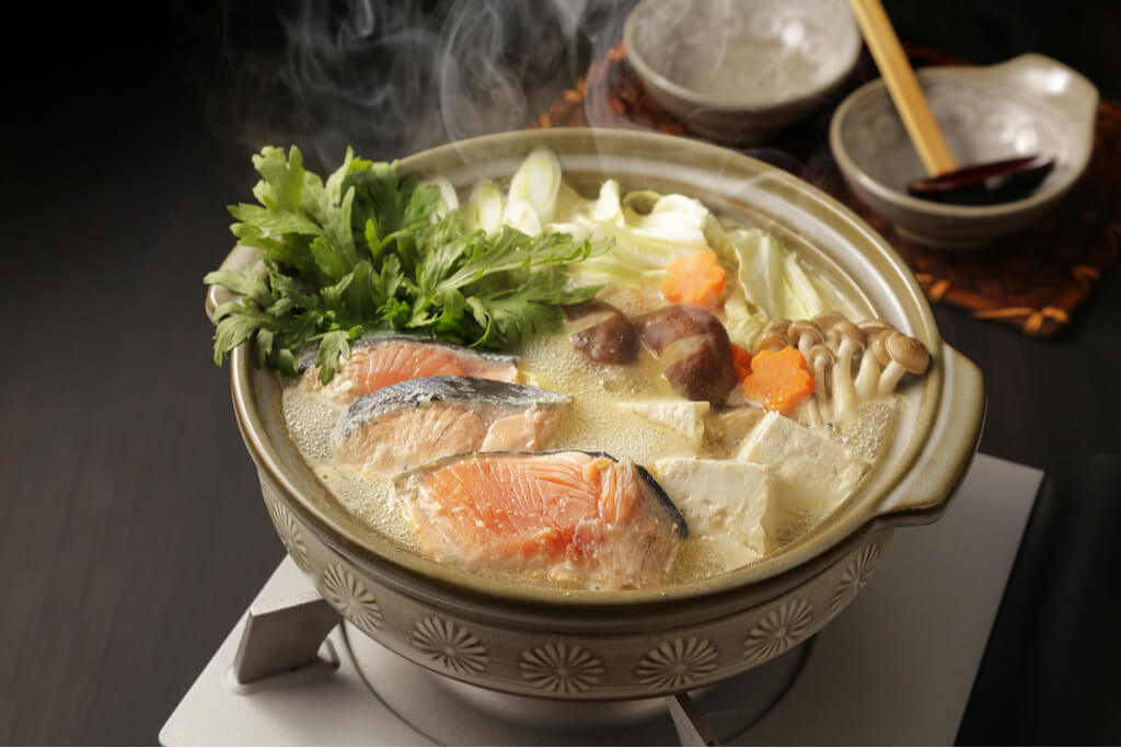 A pot of Ishikari nabe cooking on a small burner on a table with two small bowls and a traditional Japanese wooden spoon in the background