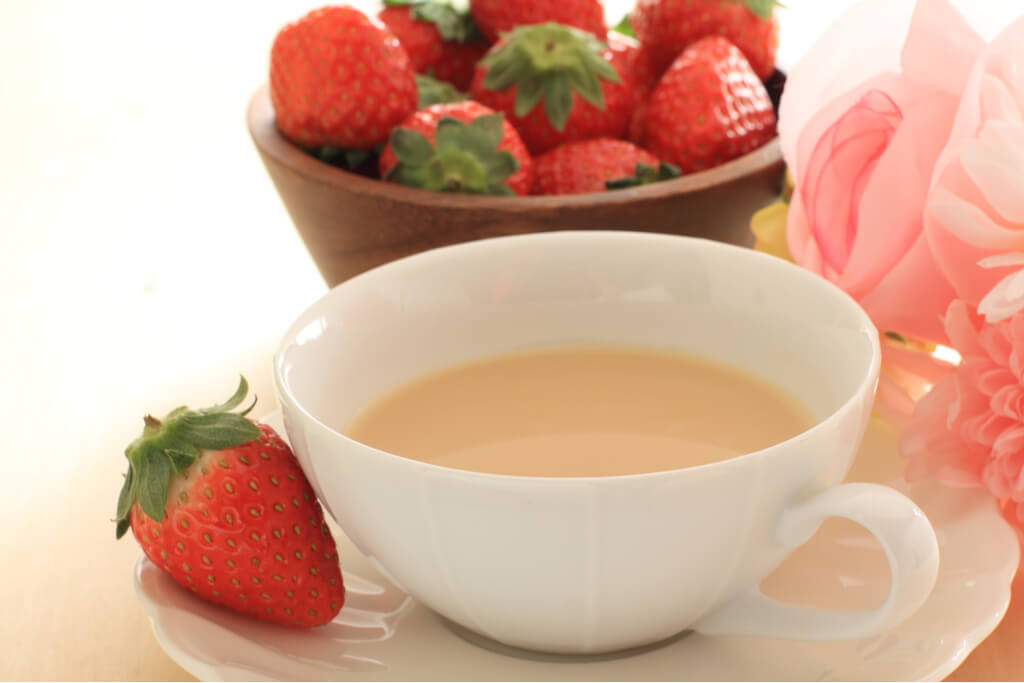 A cup of Hokkaido Milk tea on a plate with a strawberry and a bowl of Japanese strawberries in the background