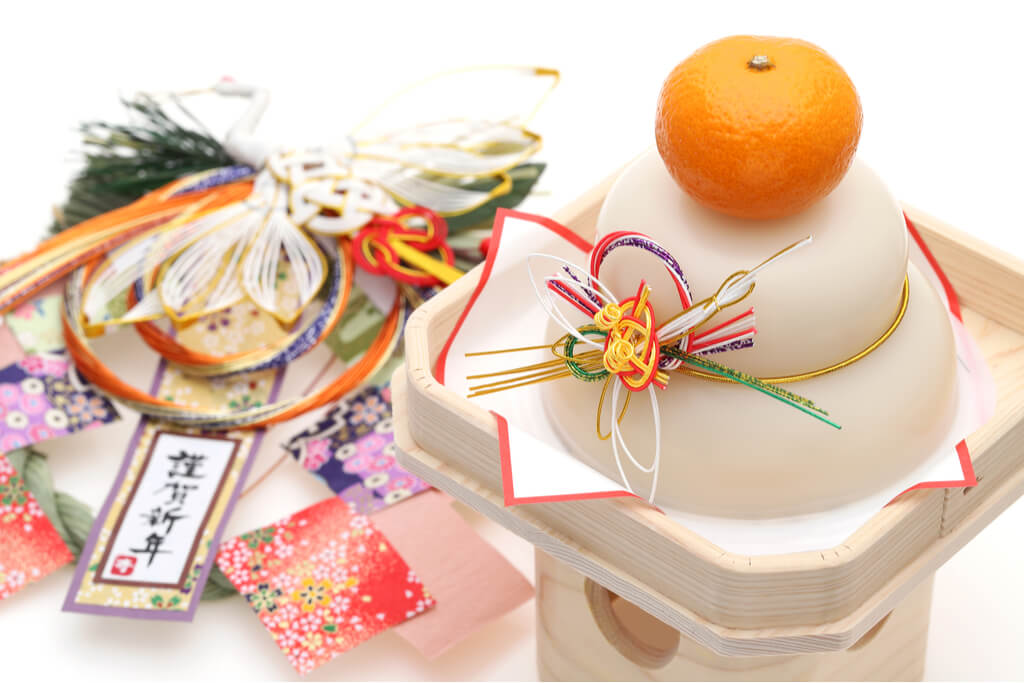 A kagami mochi, a Japanese new year food, on a pedestal next to a set of Japanese new year decorations