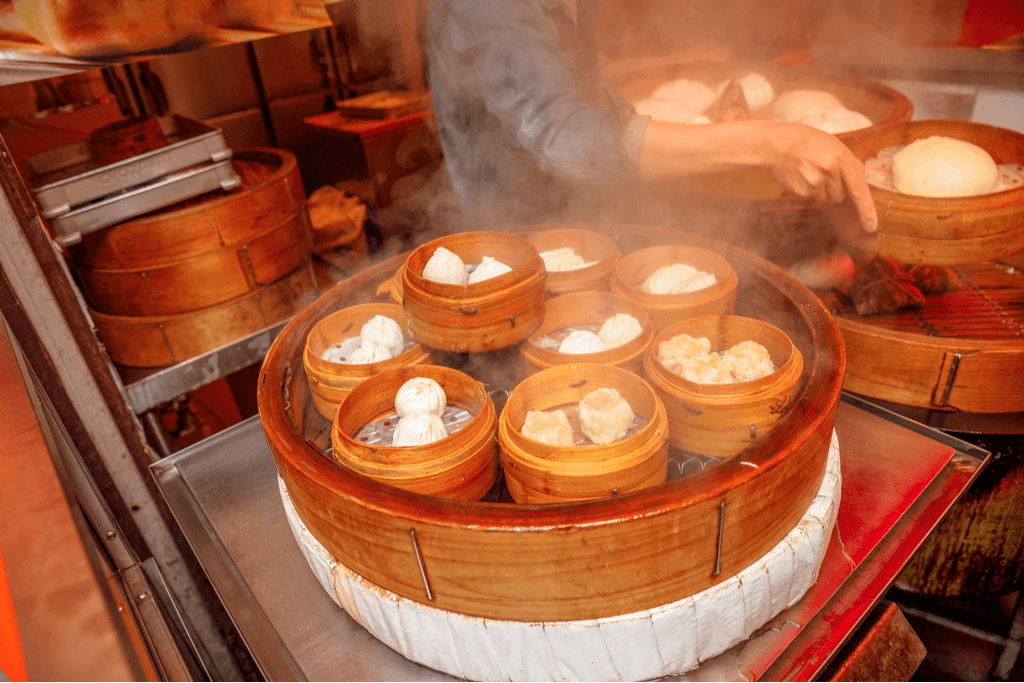 Many steamed buns being cooked at a shop in Yokohama Chinatown while the maker moves the buns around.
