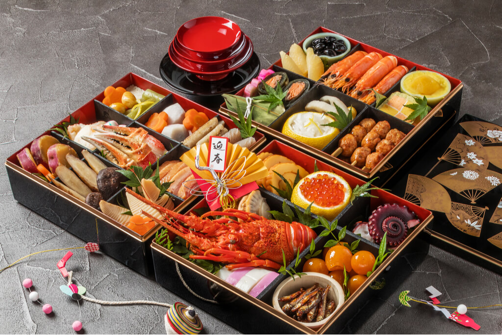 Several boxes of osechi, a Japanese new year food that comes in lacquer boxes, with many different seafoods and vegetables inside.