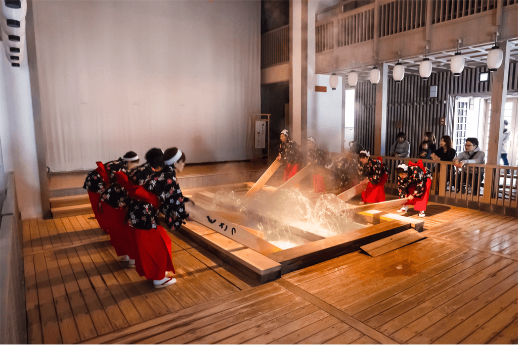 Women in traditional Japanese-style worker garbs use long paddles to splash water at the Kusatsu onsen, a popular Japanese onsen town.