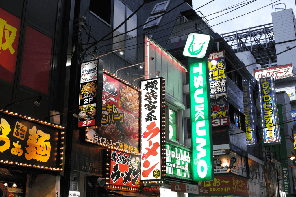 The storefront signboard of a Yokohama ramen restaurant with the words "Yokohama Iekei Ramen" written on it in front of other shops.