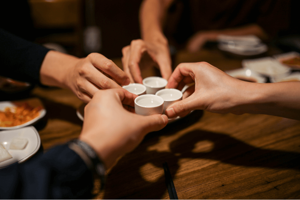 Four people cheers over a meal with small cups of Japanese sake meeting in the middle.