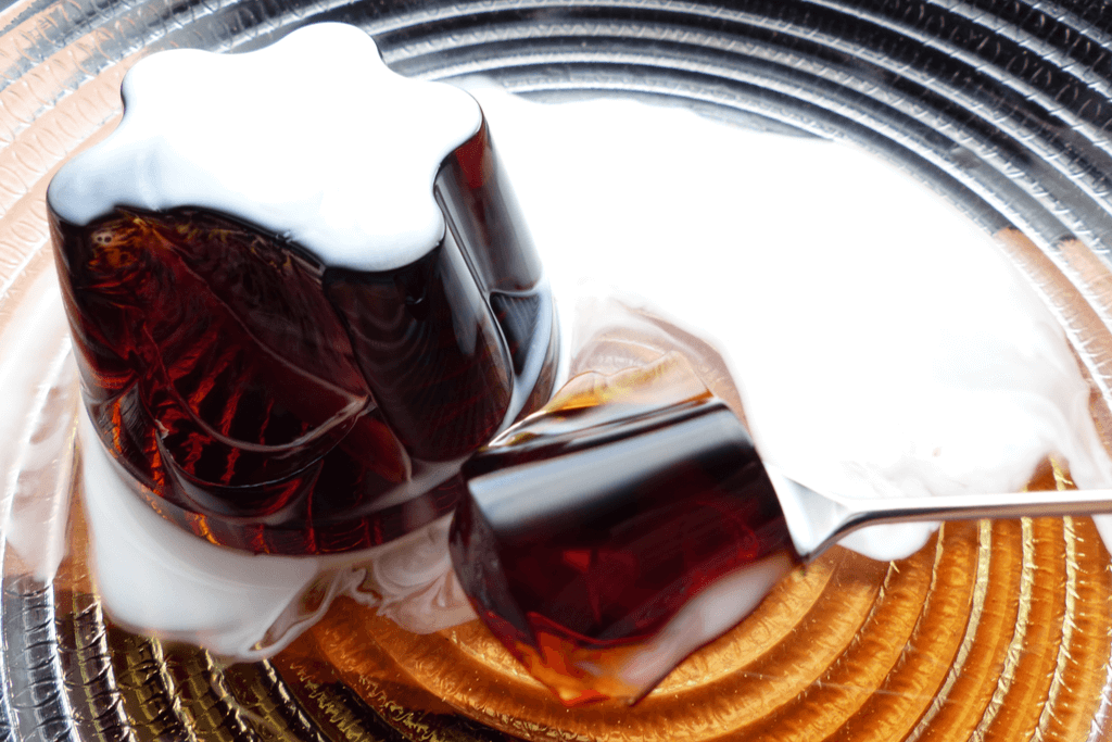 A plate of Japanese coffee jelly with white cream on top with a spoon holding a piece of the jelly.