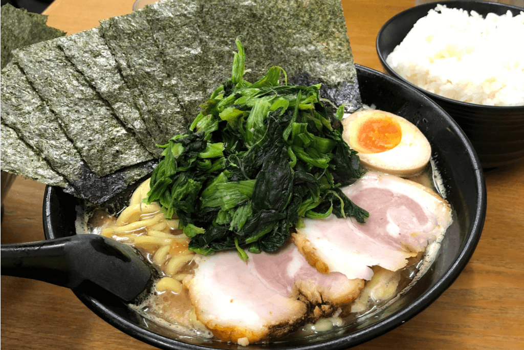 A bowl of Yokohama iekei ramen with a large pile of Japanese spinach on top and many sheets of seaweed.