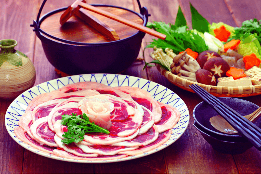 An assortment of nabe ingredients. One plate has pork meat, another bowl of vegetables and a pot.