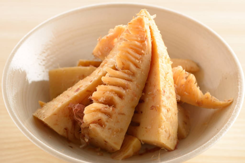 A small bowl of simmered beige bamboo shoots, mixed with pink bonito flakes.
