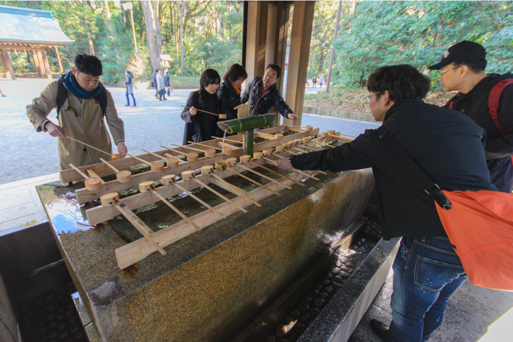 People washing their hands at a fountain, a common area in Japanese Shinto shrines, before they enter the shrine area itself.