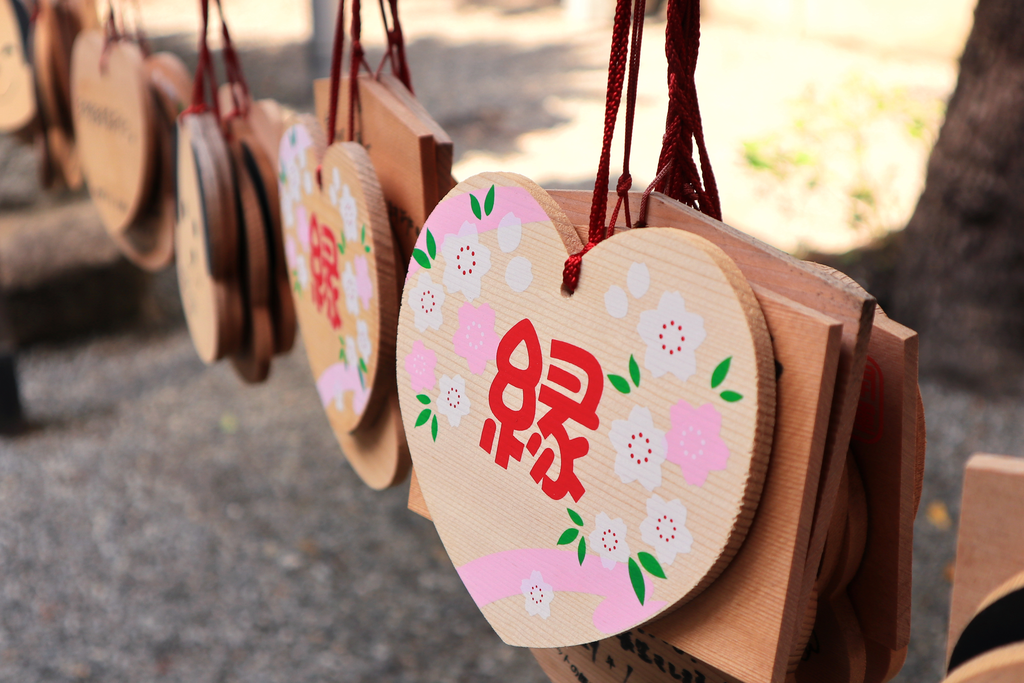 Many wooden plates hang at a Shinto shrine, with one being in the shape of a heart with a kanji meaning connection on the front.