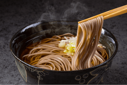 A hot, piping bowl of soba noodles being pulled out with chopsticks.