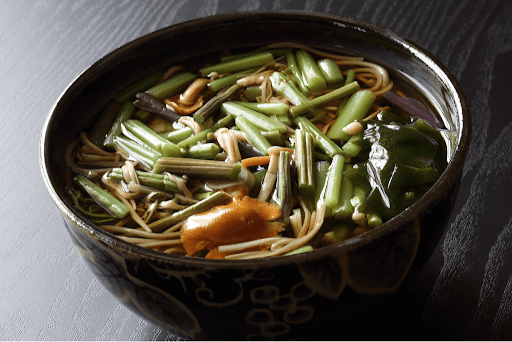 A bowl of buckwheat noodles and locally grown vegetables like green brackern ferns, bamboo shoots and brown mushrooms.
