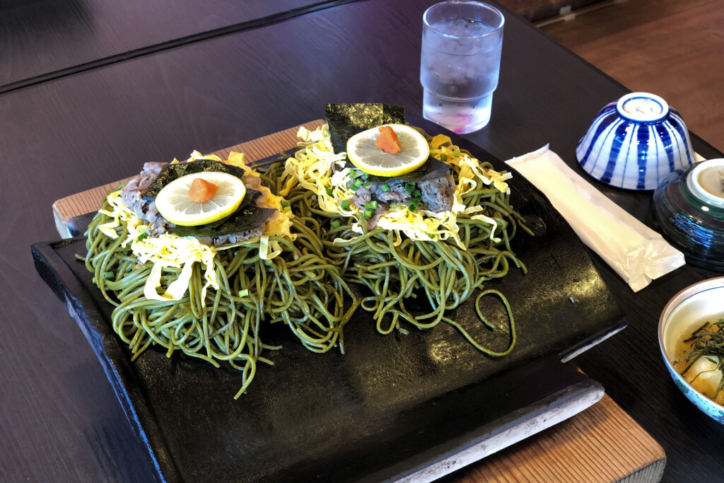 A table with green tea soba noodles on top of a roofing tile which is cooking the noodles.