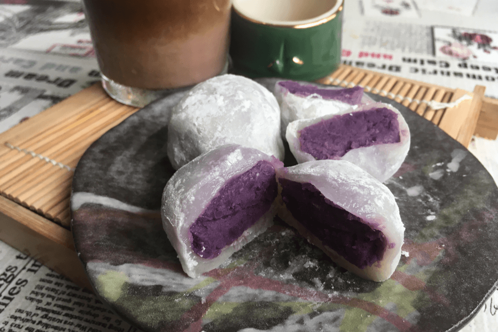 A plate on a tray with three purple potato filled daifuku next to a cup of chocolate milk.