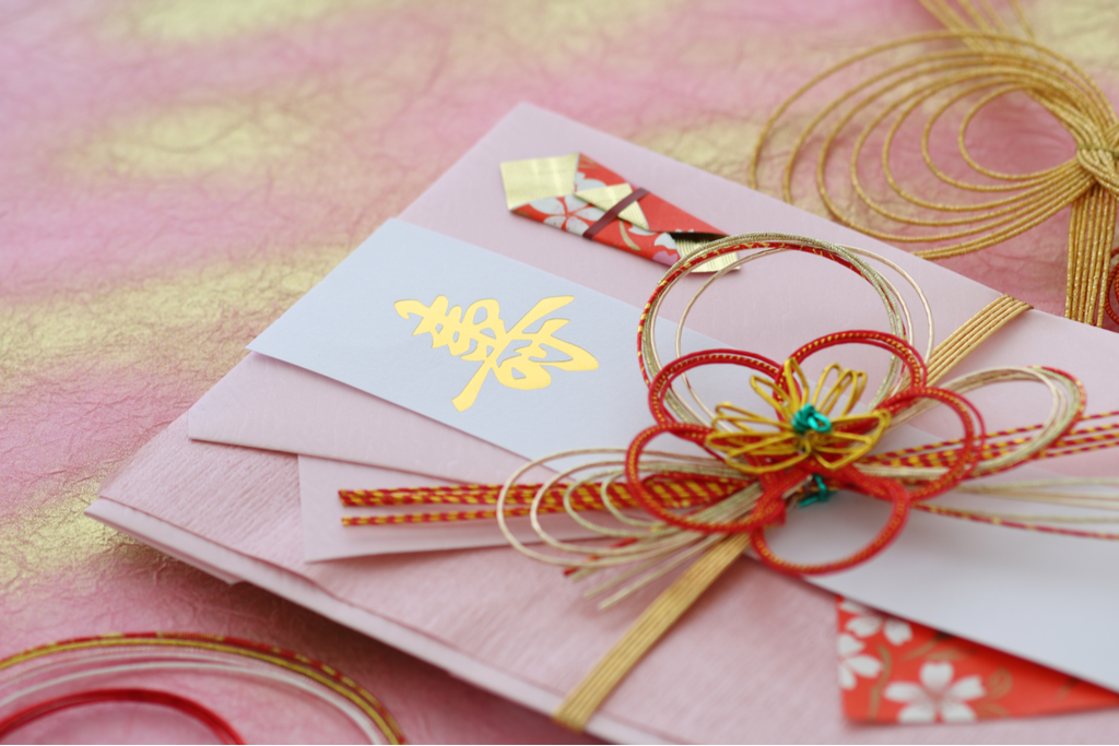 A Japanese card decorated with a traditional Japanese red, white, and gold ribbon and origami, signifying a celebration in the culture of gift giving in Japan.