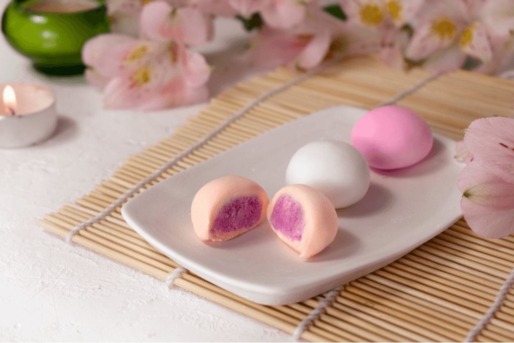 A tray with a white plate showcasing three types of daifuku, with one cut in half showing a sakura filling that's pink with a little bit of white.