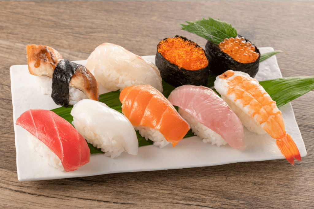 Nine pieces of sushi, seven of which are nigiri and two are warship rolls, on a white plate on a table
