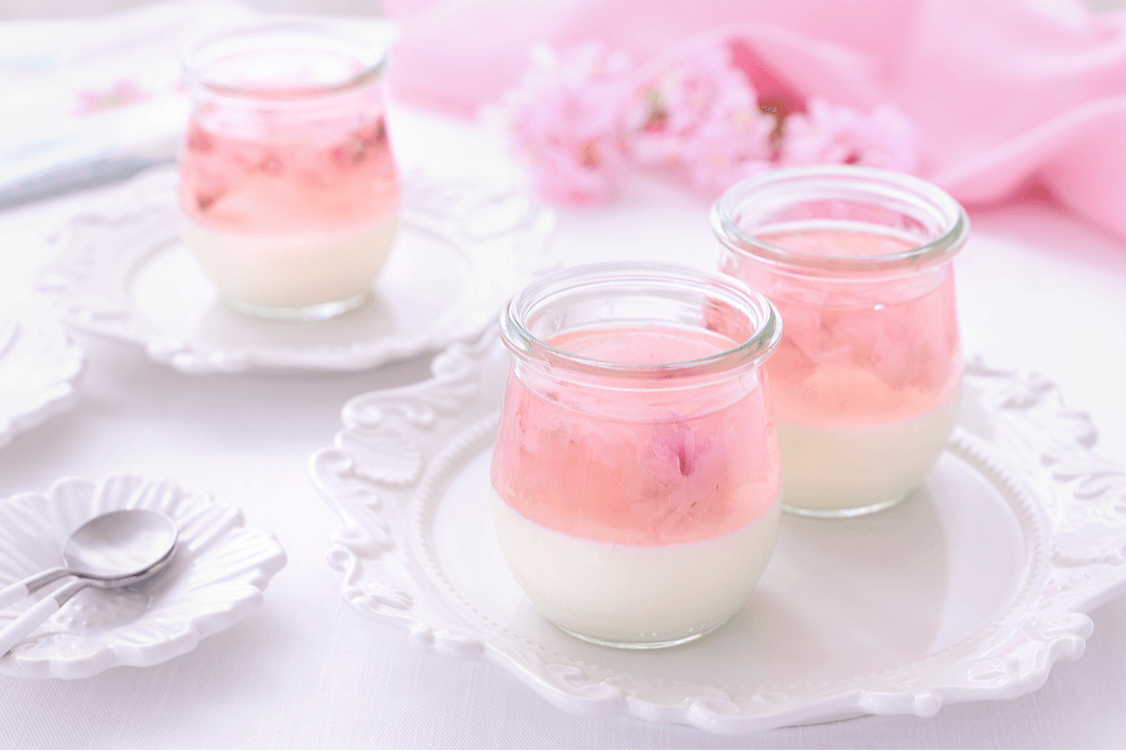 Small cups of Japanese milk pudding with cherry blossom jelly on top, one of the popular sakura-flavored snacks, on plates with cherry blossoms in the background.